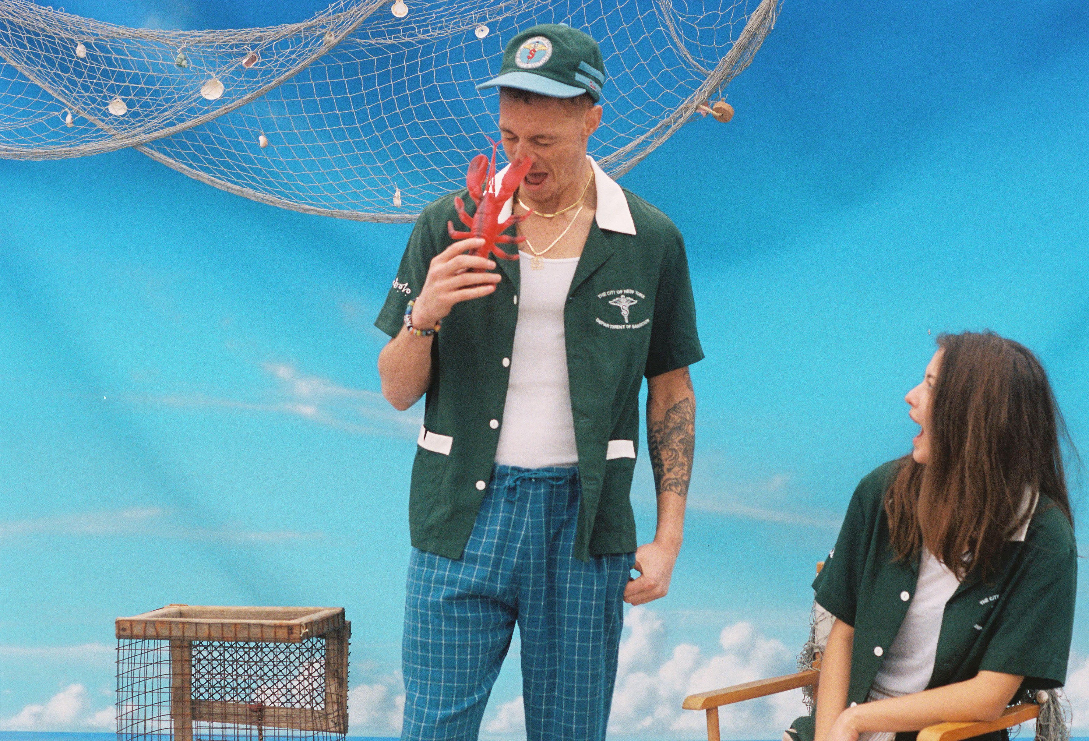 Male model in shirt holding up a toy lobster pretending to get pinched on the nose while a female model looks on