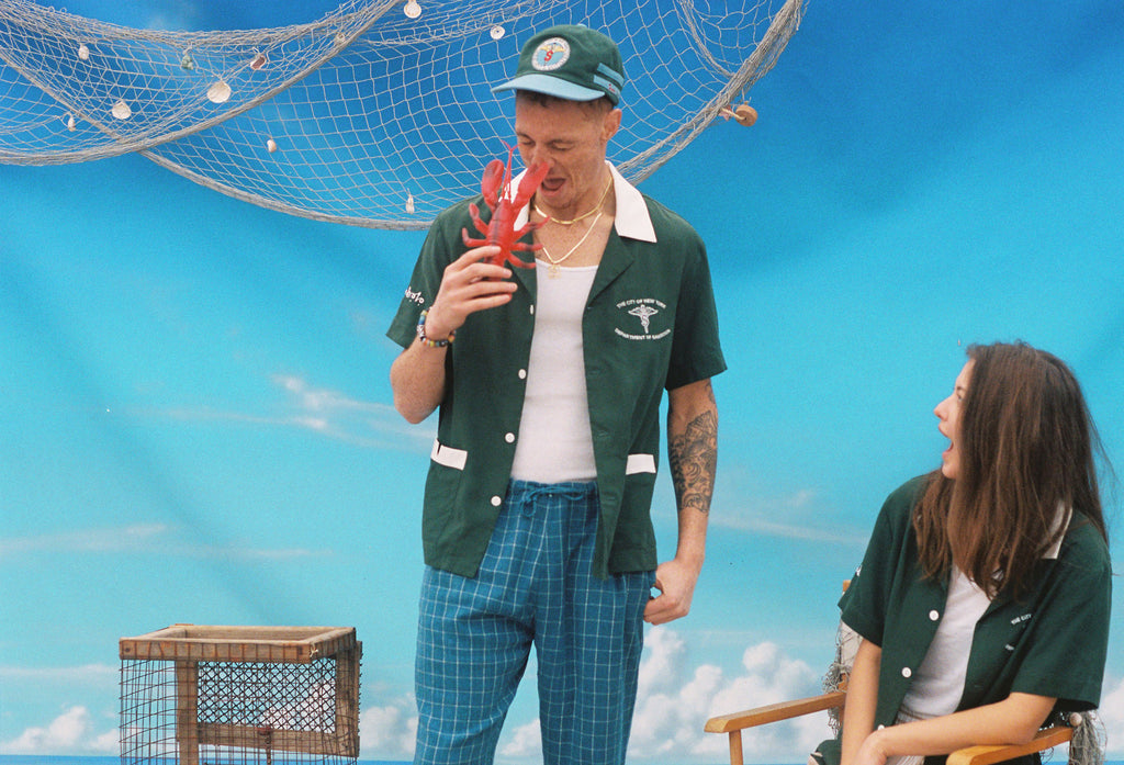 Male model in shirt holding up a toy lobster pretending to get pinched on the nose while a female model looks on