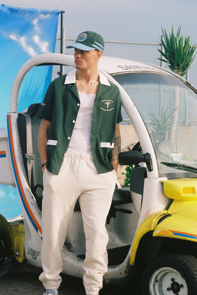 Male model leaning on a sanitation car in the shirt over an otherwise all white outfit
