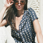 Female model wearing shirt sitting in white pants and sunglasses