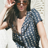 Female model wearing shirt sitting in white pants and sunglasses