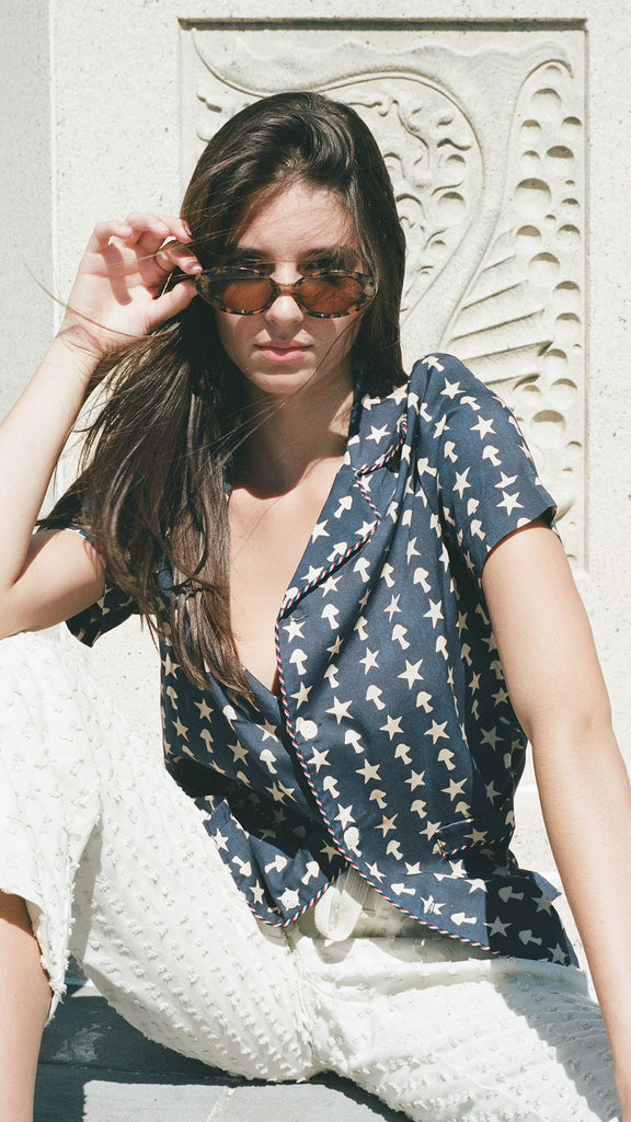 Female model wearing shirt sitting in white pants and sunglasses