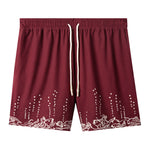 Maroon swim trunks with embroidered fish and mermaids at the leg openings with white bubbles climbing up the legs