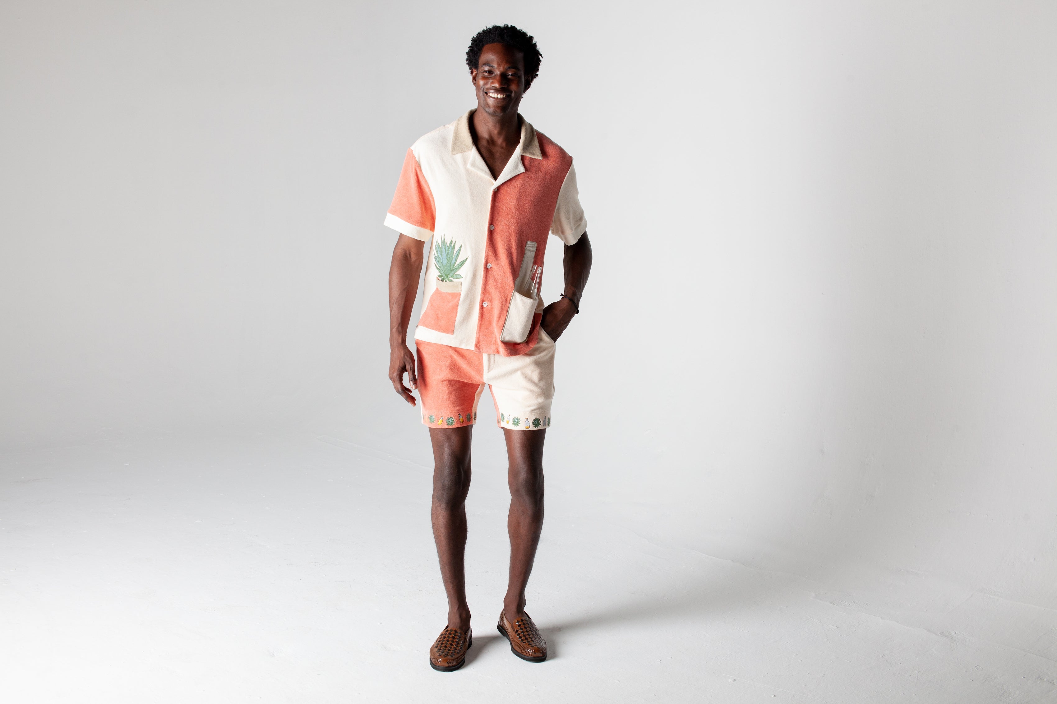 Full body image of male model wearing the Gusanito cabana set, with an empty tequila bottle in the outer right pocket